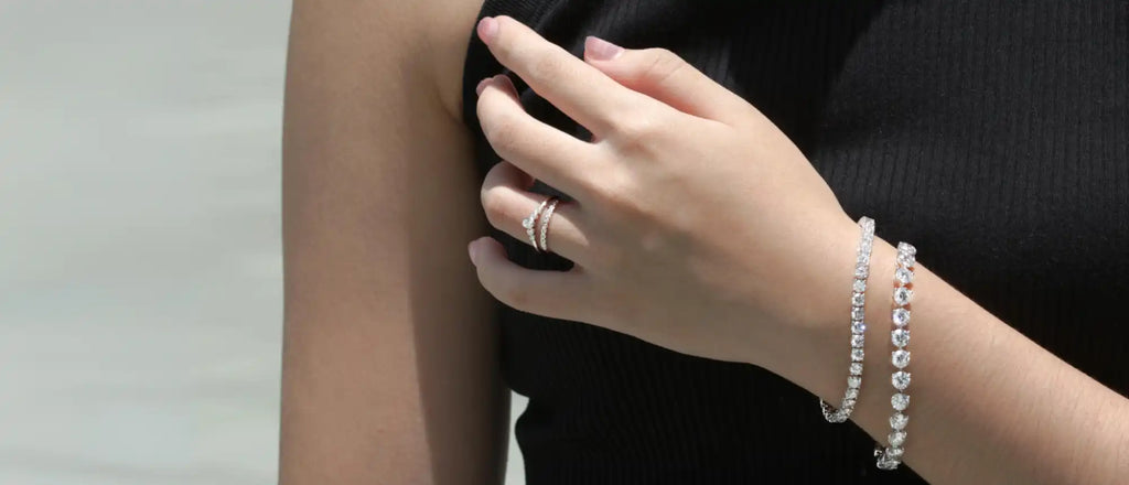 A delicate silver tennis bracelet adorns a hand wearing a ring.