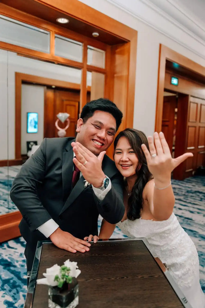 A newly married couple showing off their wedding rings with joyful expressions.